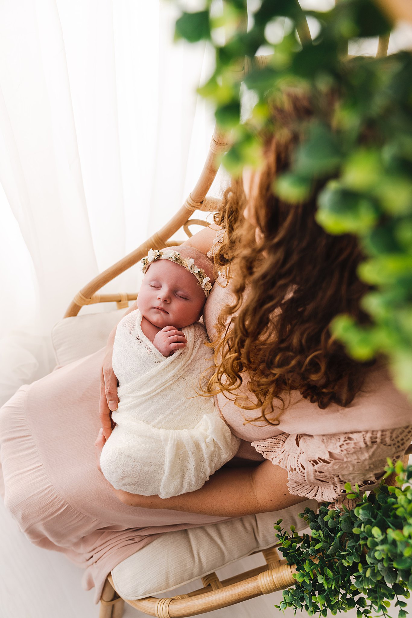 newborn sleeps swaddled in mom's lap in a wicker chair