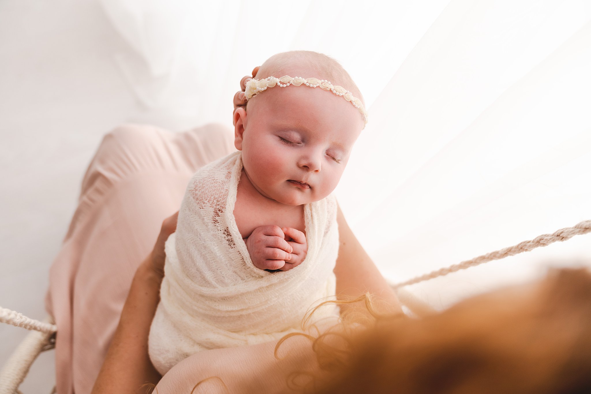 Newborn baby sleeps swaddled in her mothers hands in a studio home birth midwives