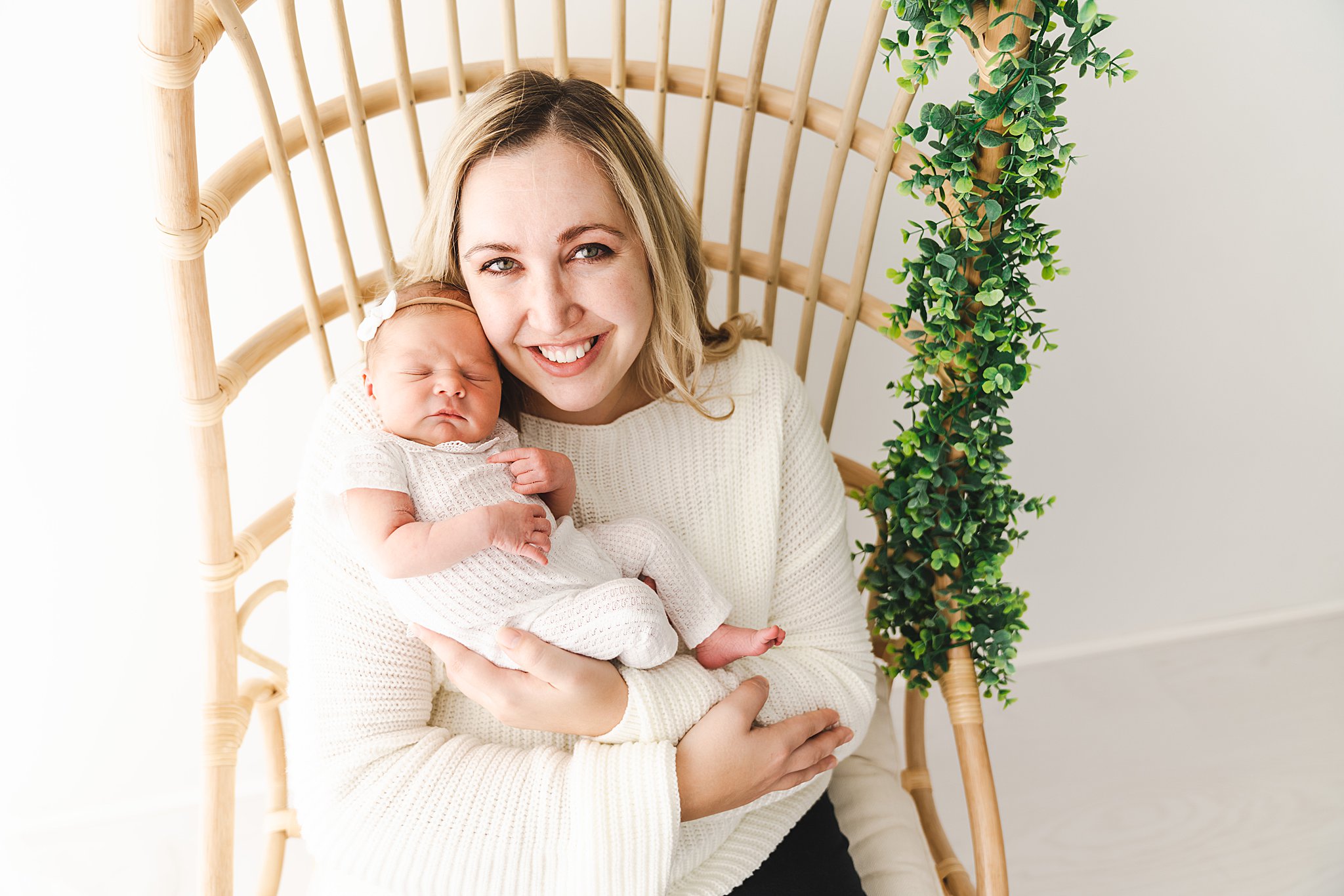 mother sits in a wicker chair in a studio while holding her newborn minneapolis birth center