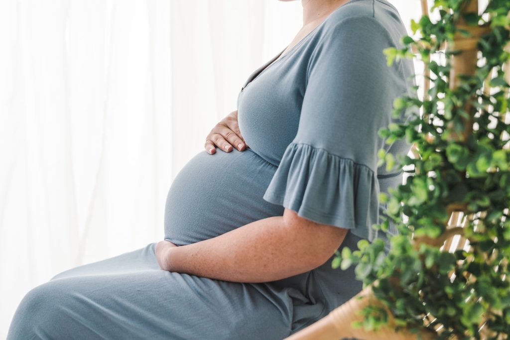 Silhouette of a mother to be sits in a chair in a studio