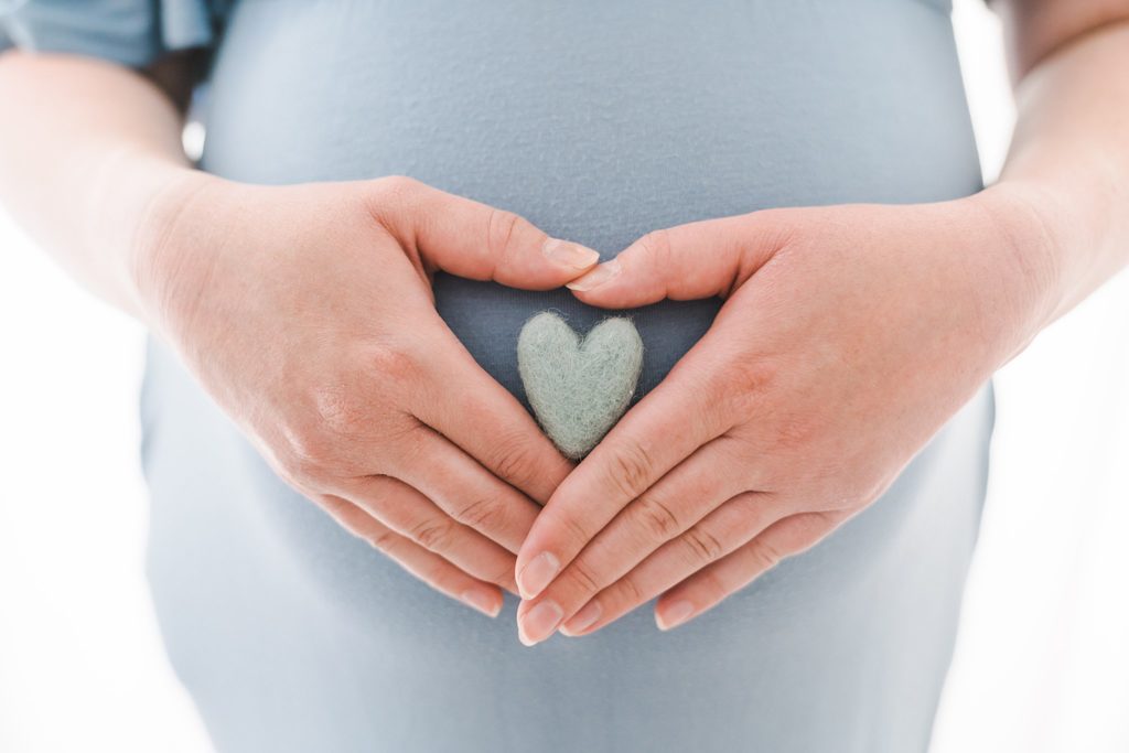 Mother-to-be holds a felt heart on her bump with hands in the heart shape twin cities midwives