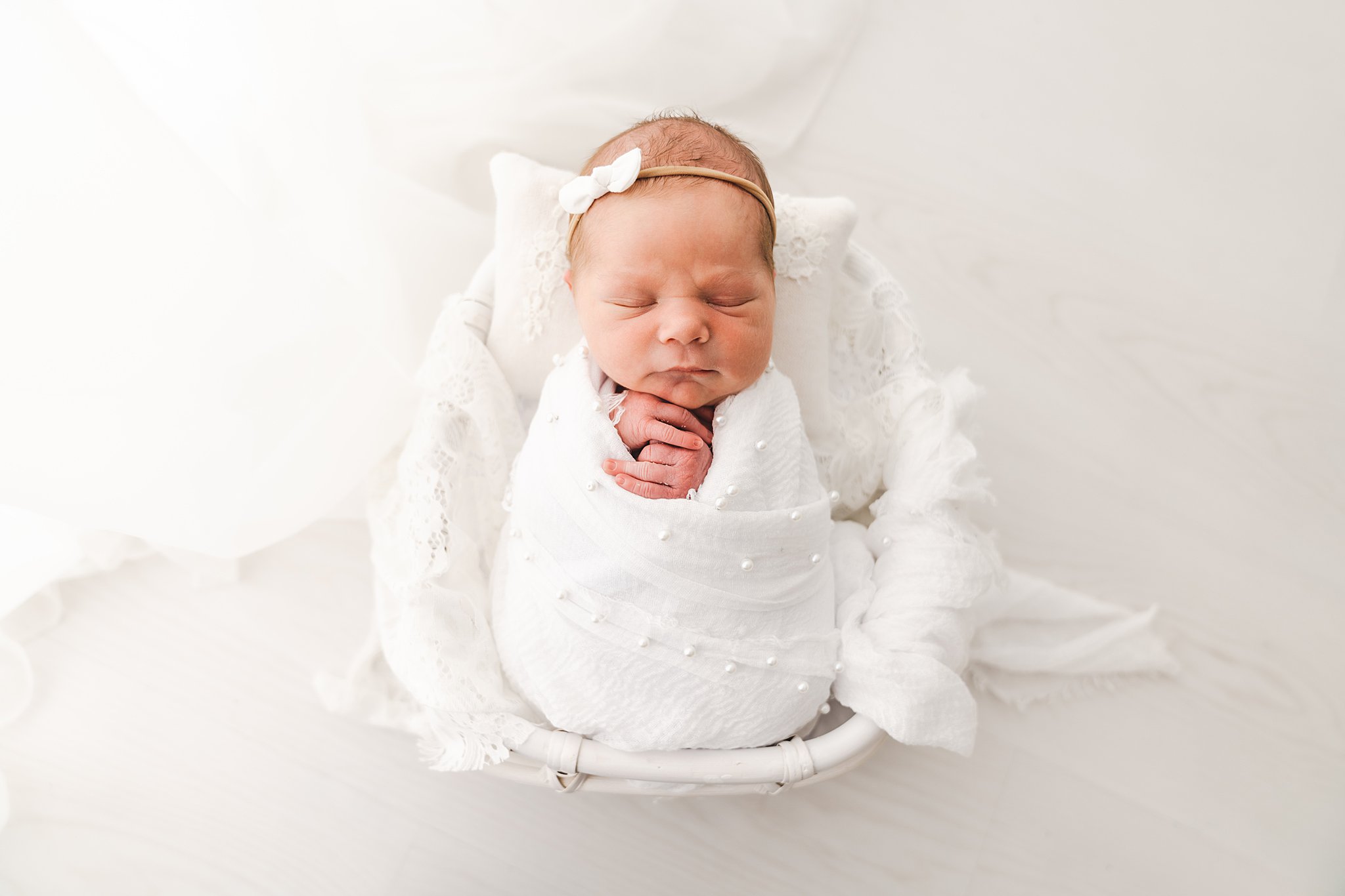 Newborn baby sleeps in a white swaddle and white wicker basket in a studio minneapolis baby boutiques