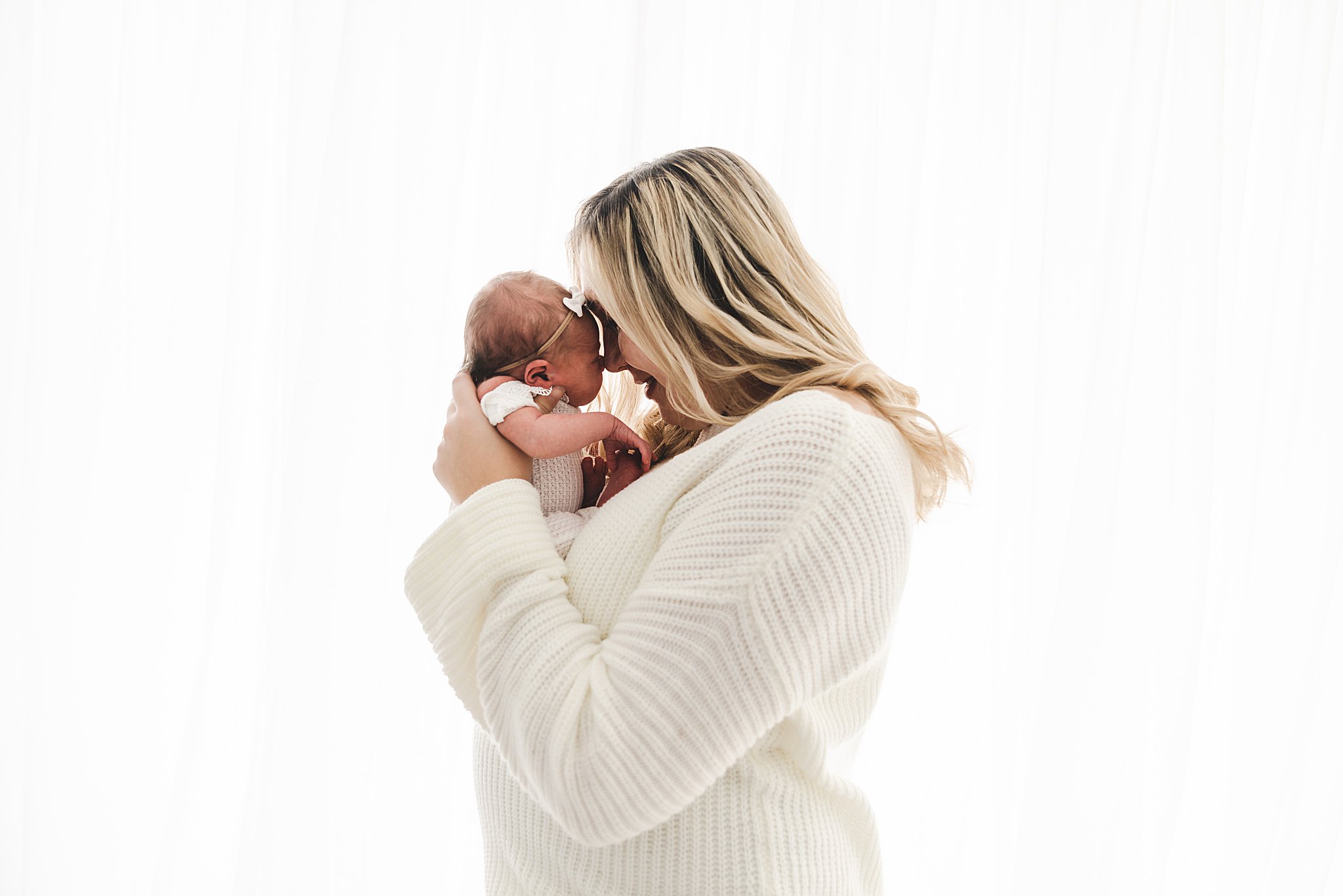 A new mother nuzzles forehead to forehead with here newborn baby girl in front of a window in a studio twin cities midwifery