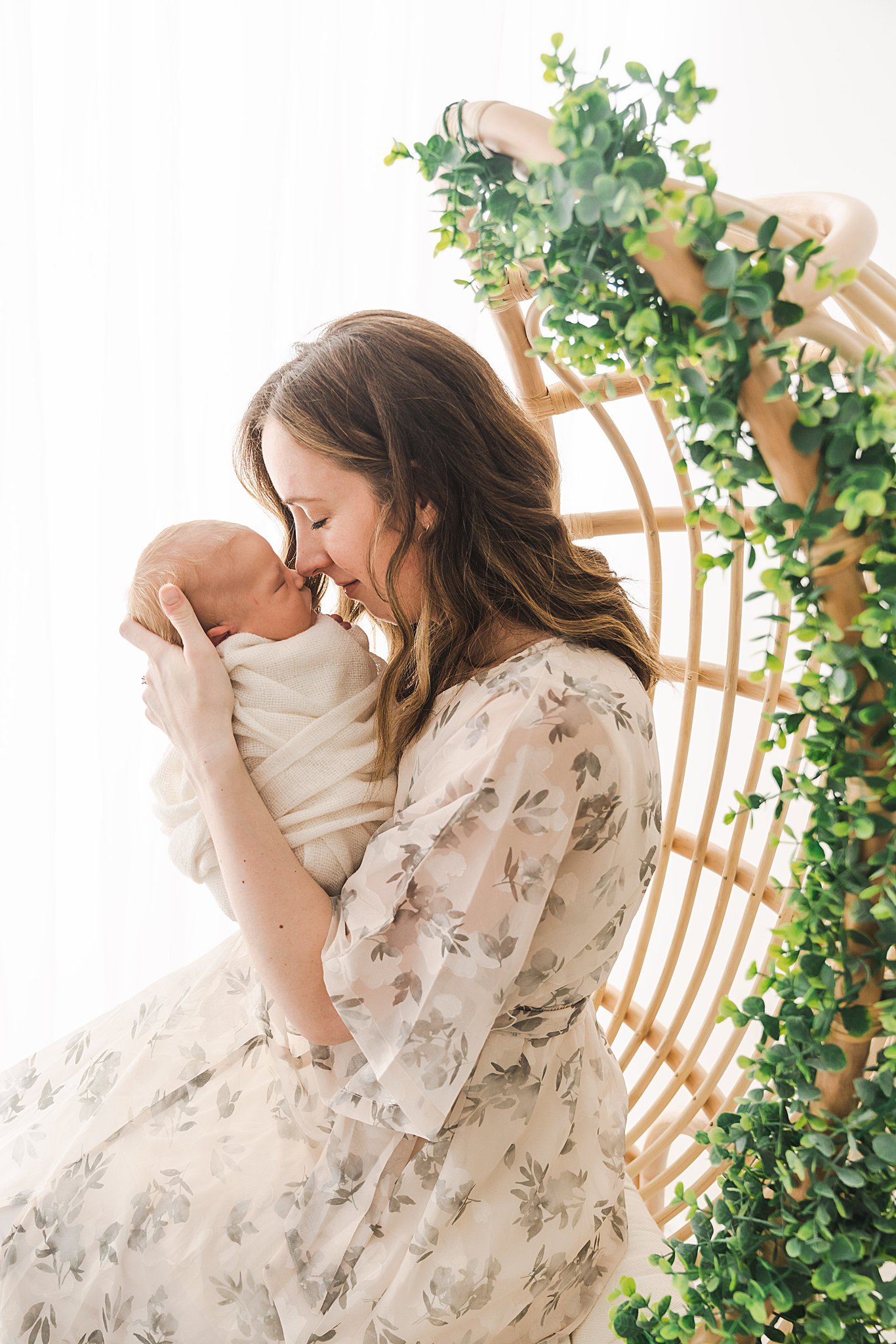 A mother in a floral white dress presses her nose to her newborn baby's nose baby grand minnesota