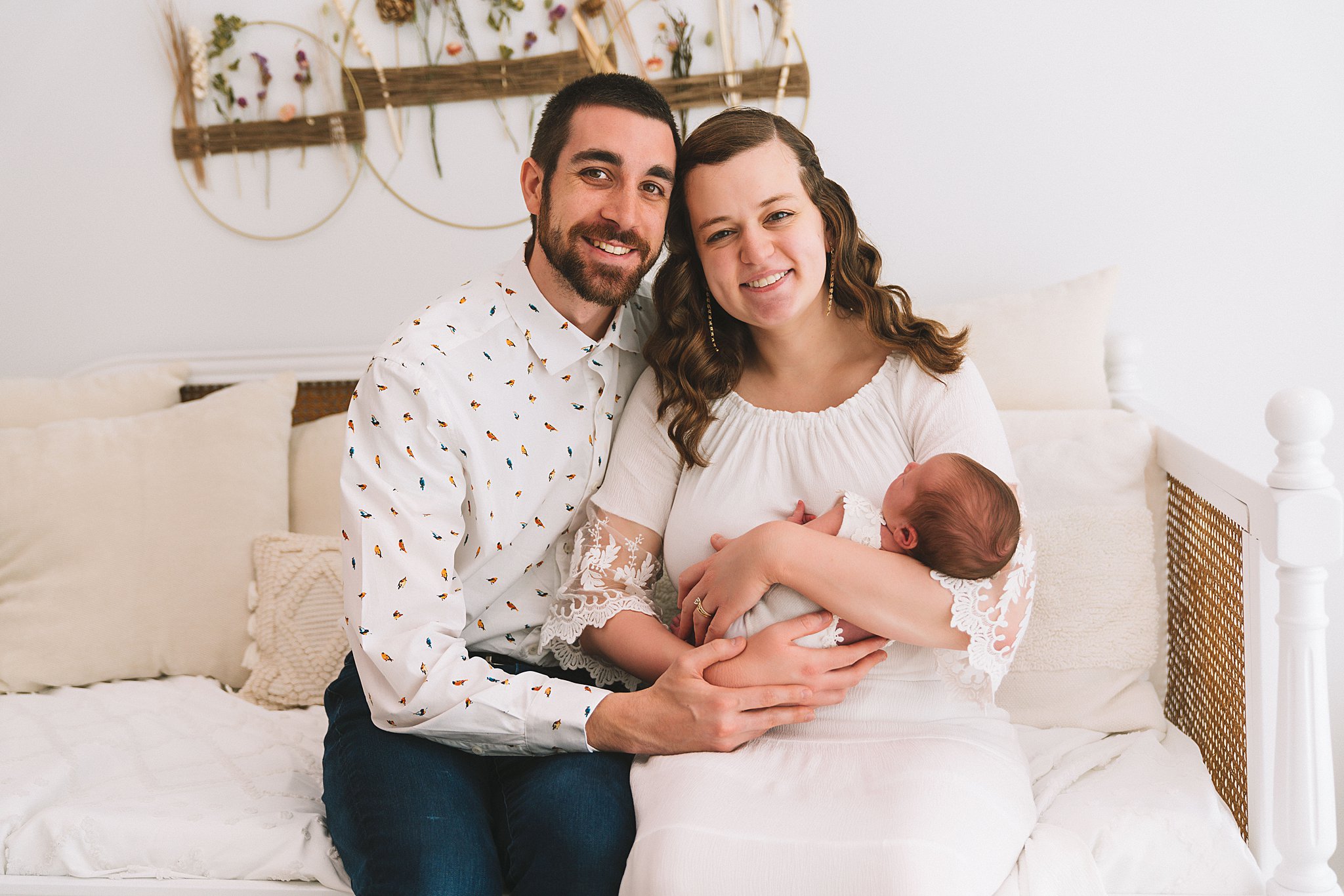 New parents sit on a couch in a studio while holding their newborn baby