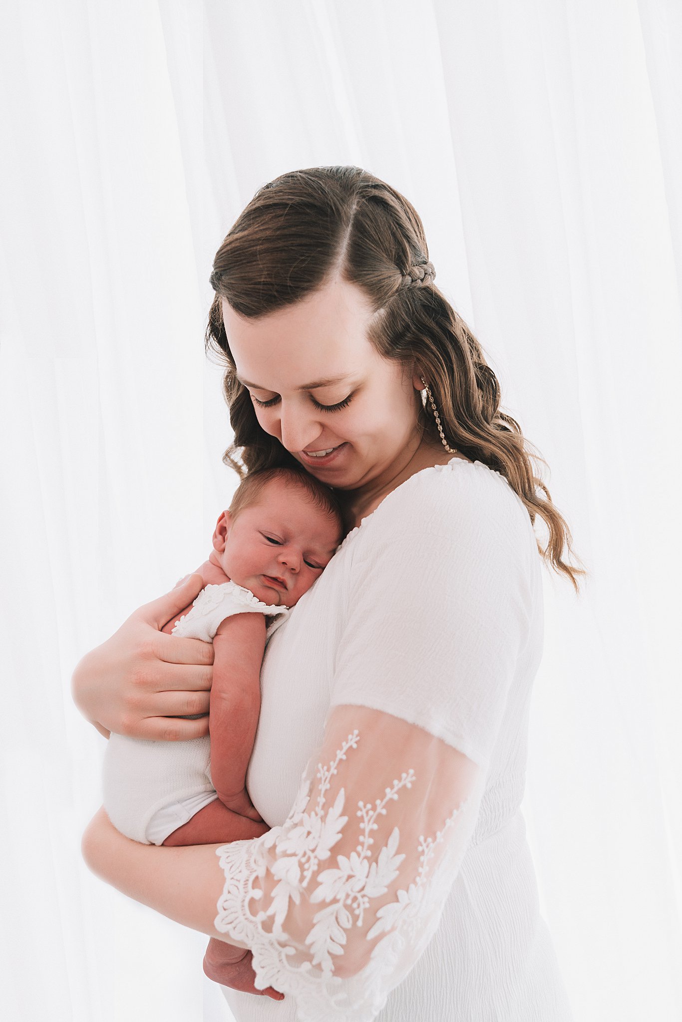 A new mother stands in front of a window while holding her sleeping newborn baby against her chest bumbelou