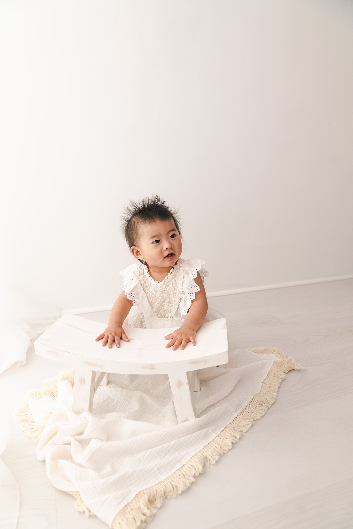 A young toddler plays with a white wooden bench next to a window in a studio