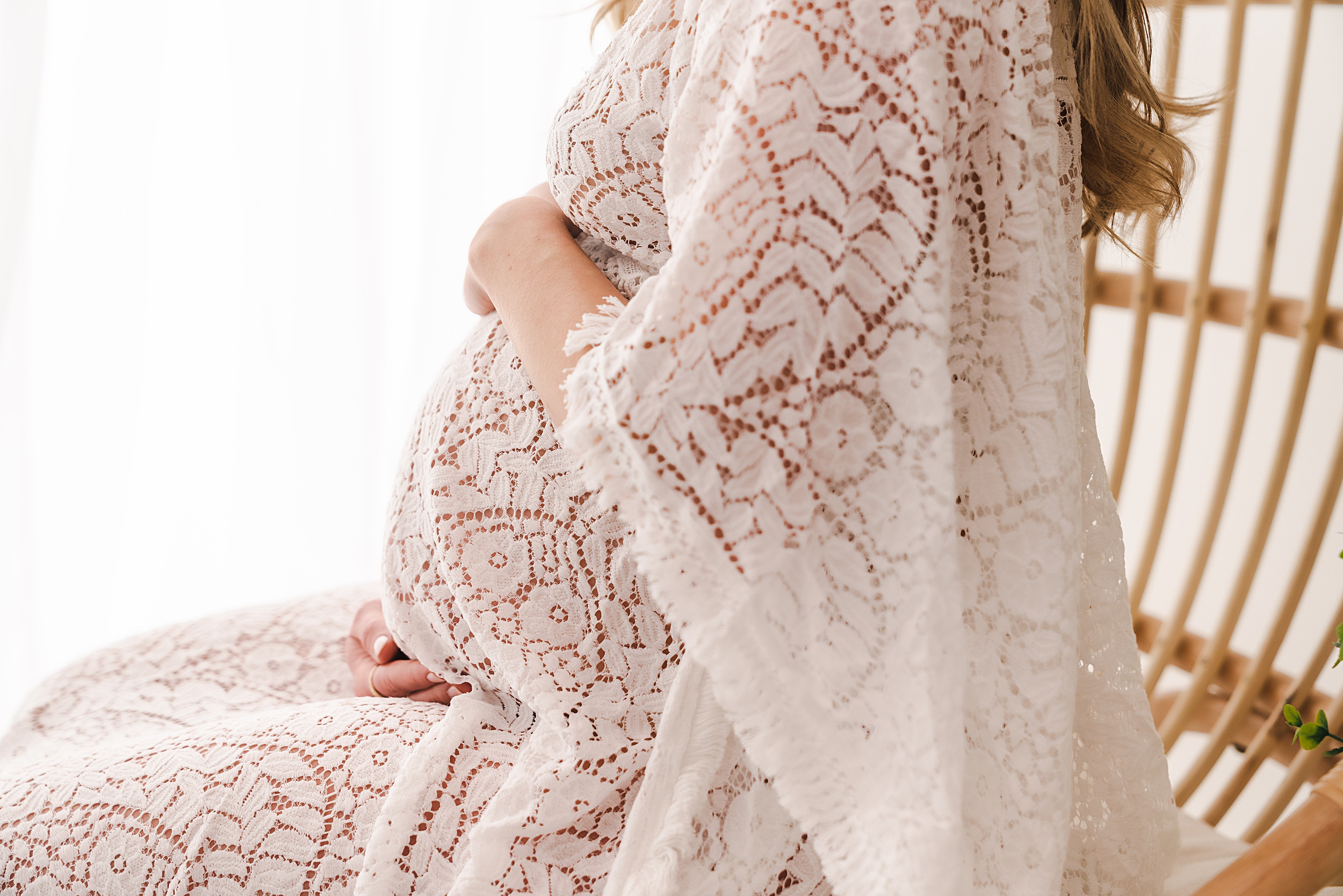 Details of a pregnant woman sitting in a wicker chair holding her bump mother baby center minneapolis