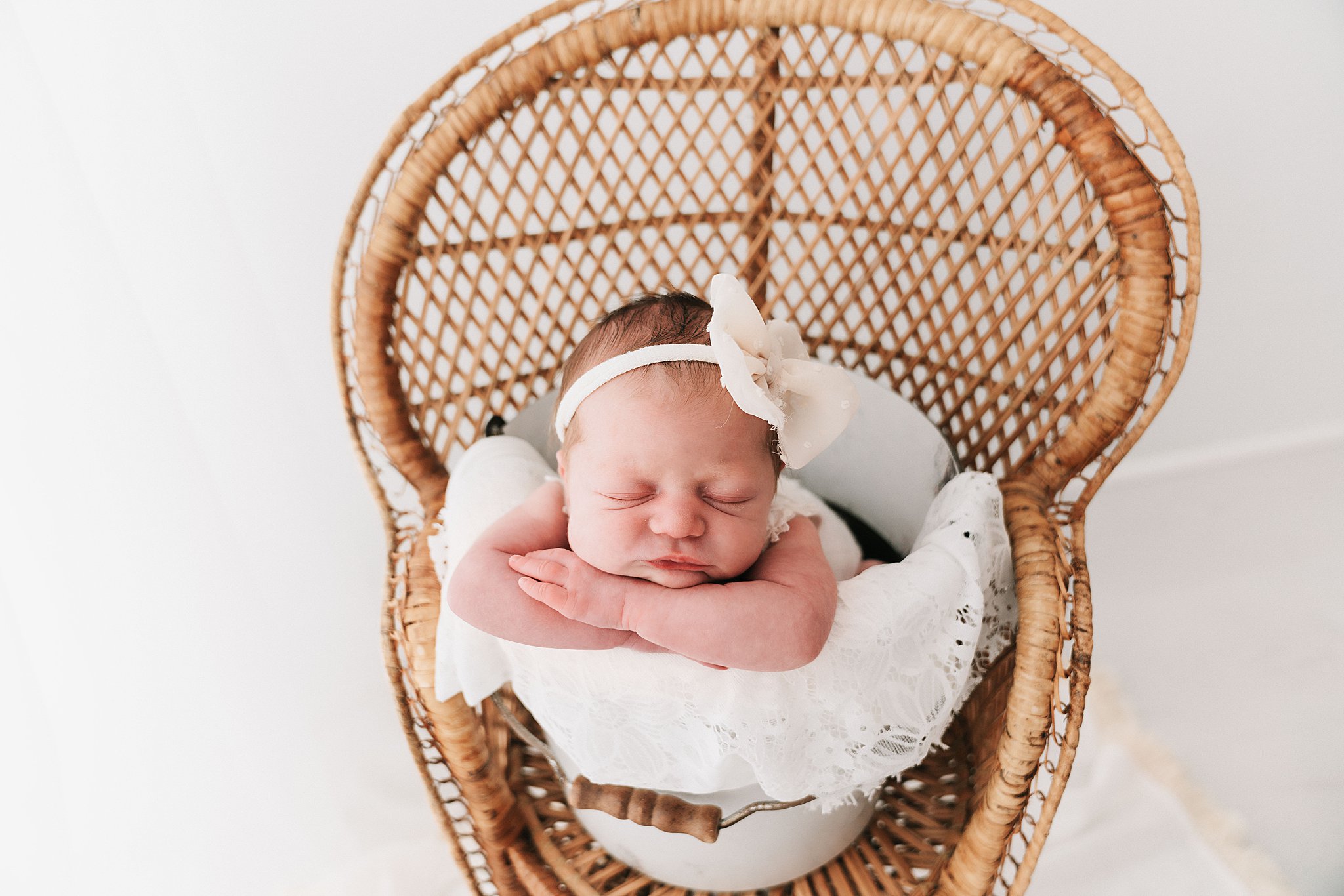 A newborn baby sleeps on her arms in a bucket sitting on a wicker chair pacifier minneapolis