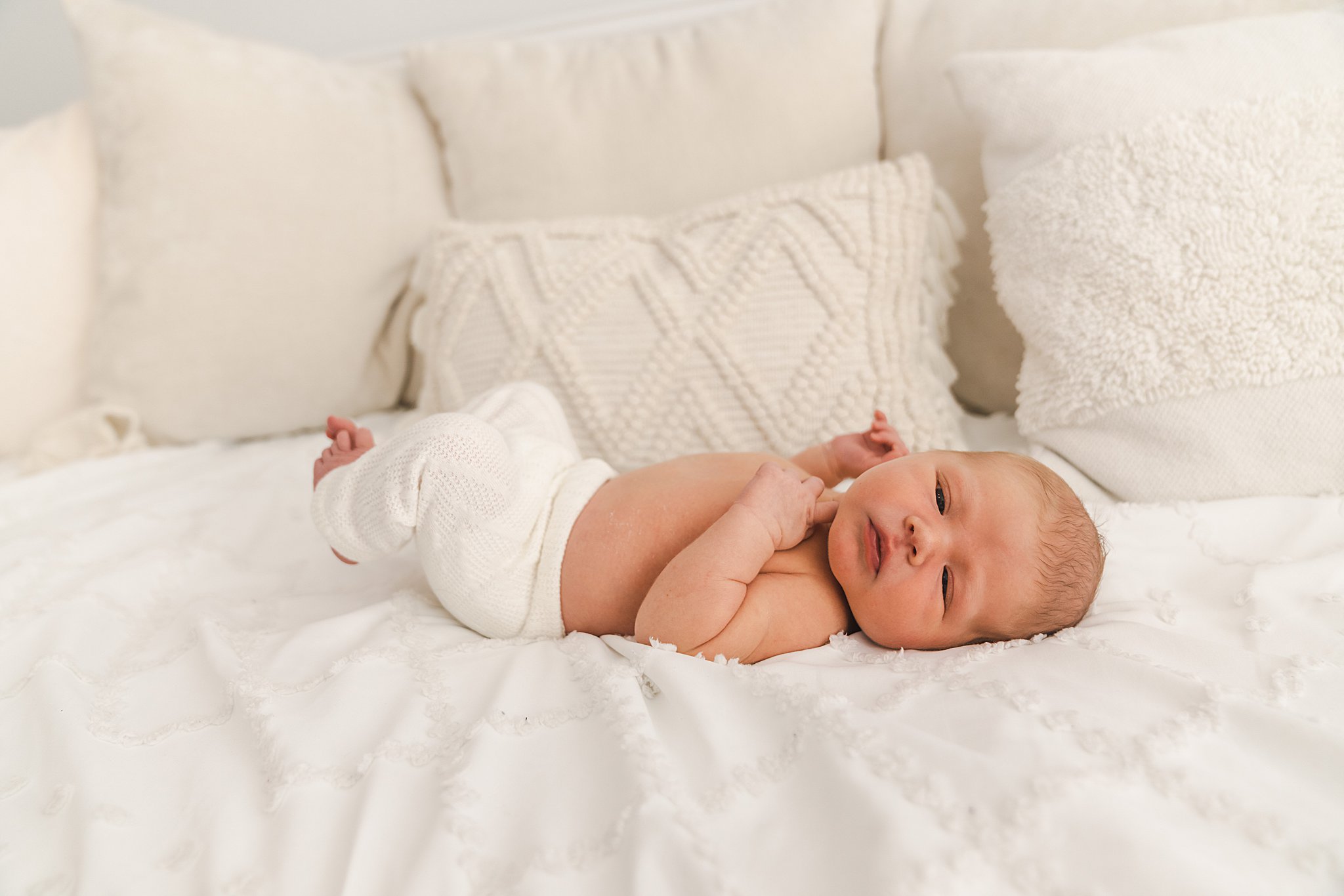 A newborn baby lays on a bed in knit white pants with eyes open moon and stars boutique