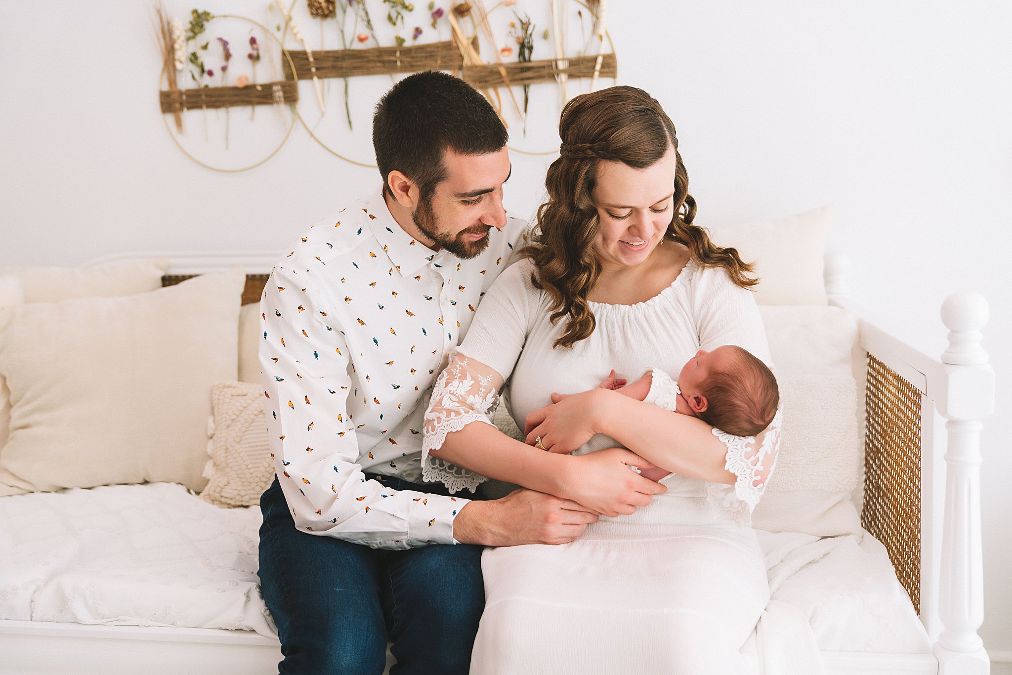 A mother and father sit on a couch together looking down at their newborn daughter in mom's arms