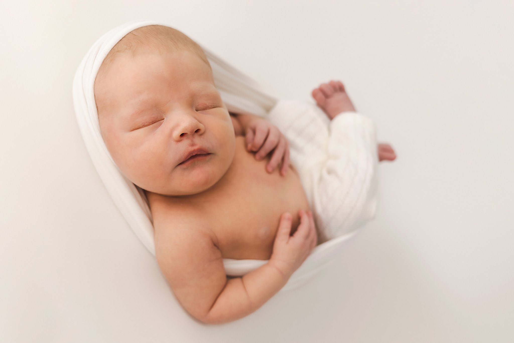 A newborn baby sleeps in white pants in a white swaddle north star newborns