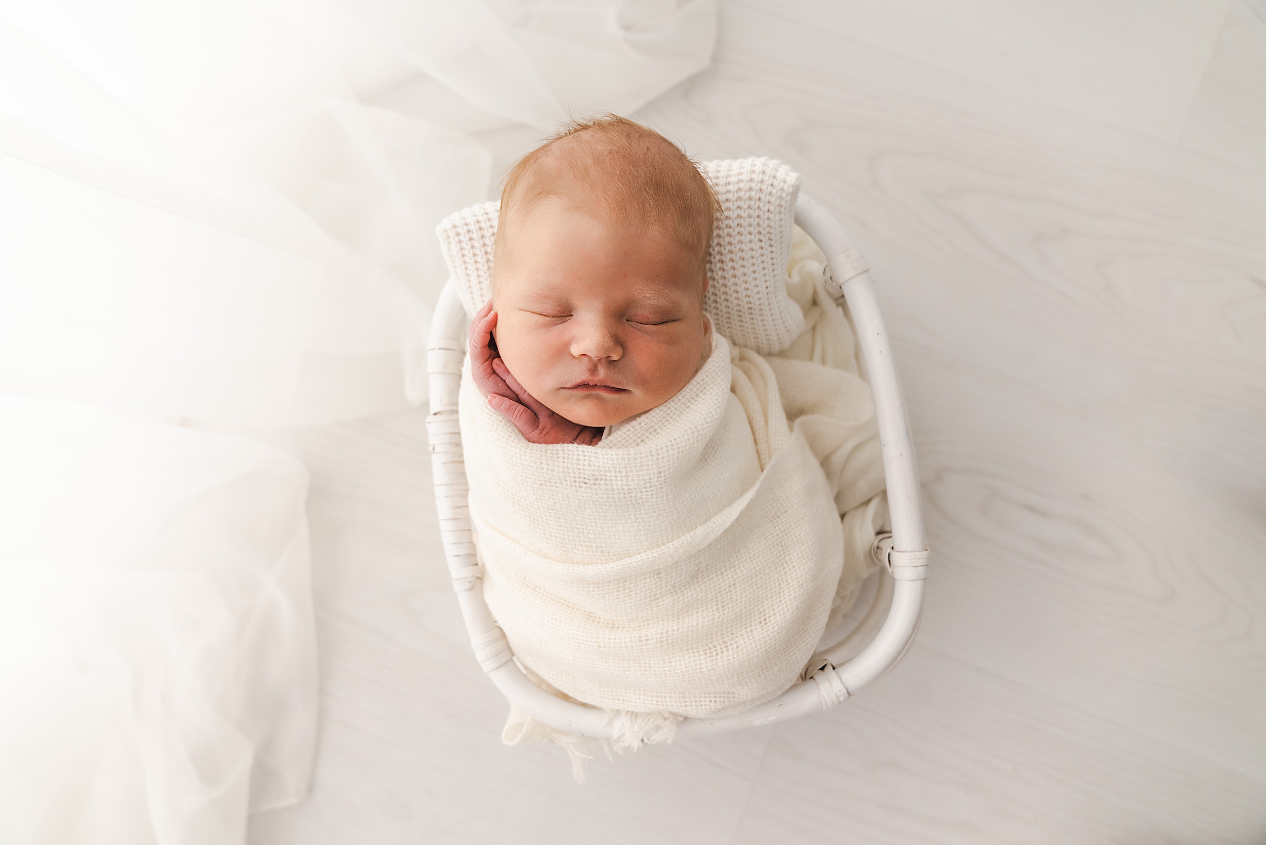 A newborn baby sleeps in a white wicker basket