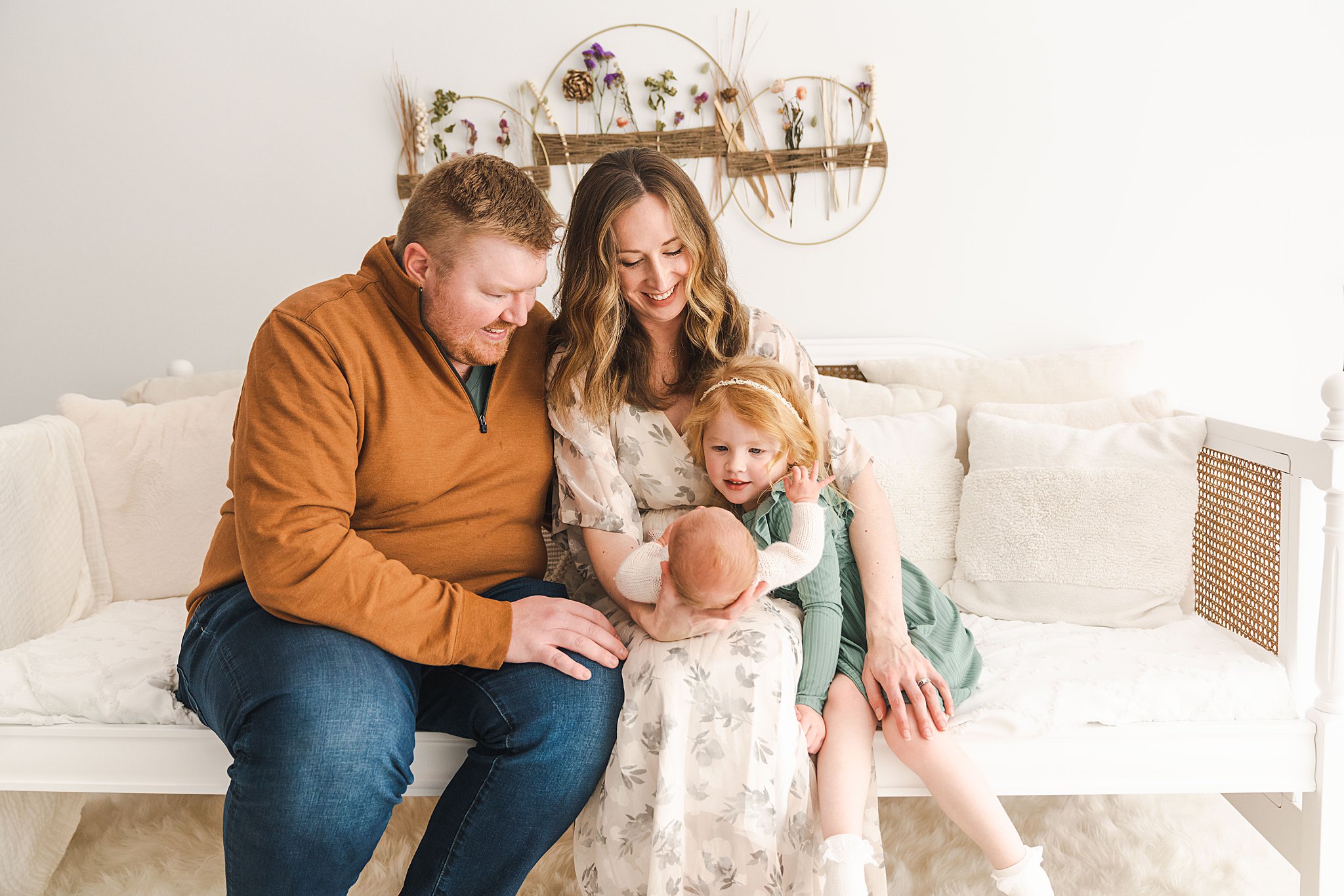 A mother and father sit on a couch with their toddler daughter as they all look down at the newborn baby in mom's lap birthed mn