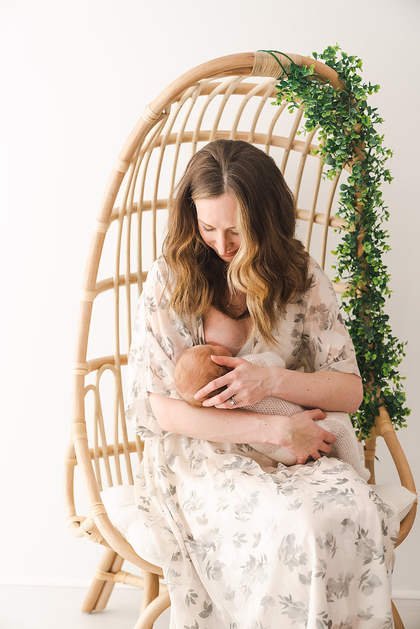 A mother breastfeeds her newborn baby while sitting in a tall wicker chair