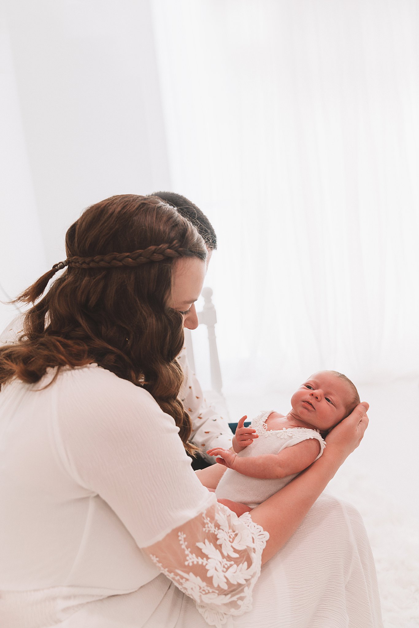 A mother sits on a bed by a window looking down at her newborn baby in her lap everyday miracles minneapolis